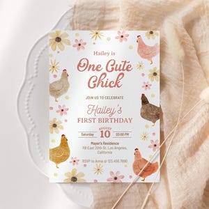 Könnte beinhalten: Eine weiße Geburtstagseinladungskarte mit dem Text "One Cute Chick" und "Hailey's First Birthday". Die Karte zeigt Illustrationen von Hühnern und Blumen in Rosa, Gelb und Braun. Die Karte liegt auf einem weißen Teller und einem beigen Tuch.