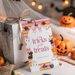 May include: A rectangular gift tag with a pink bow at the top, featuring horizontal orange, yellow, and pink stripes. The text reads "no tricks just treats" and "FROM HAILEY". Illustrations include white ghosts, black cats, and bats with pink bows.