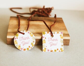 Può includere: Due etichette regalo con cordino marrone, una rotonda e una quadrata, entrambe con un design floreale e di anatroccoli. Le etichette riportano la scritta "Thank You!" in corsivo rosa. Le etichette sono su un blocco di legno.