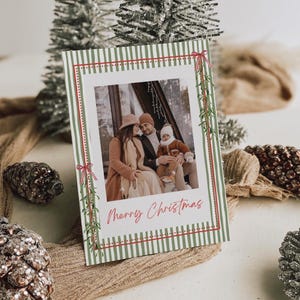 Puede incluir: Una tarjeta de felicitación navideña rectangular con un borde de rayas verticales verdes y blancas, detalles en rojo e ilustraciones de muérdago. El centro muestra una foto de tres personas, con el texto Merry Christmas en cursiva roja.