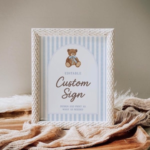 May include: A framed sign with a white textured frame. The sign has a blue and white striped background with a brown teddy bear illustration and the words "Custom Sign". The sign also includes the text "Design and print as many as needed".
