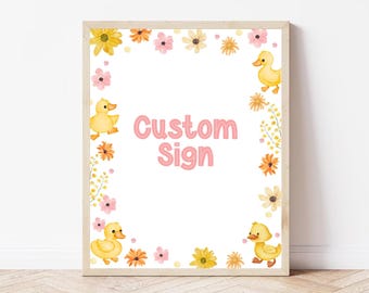 May include: A framed custom sign with a white background, featuring the text "Custom Sign" in pink. The sign is decorated with yellow ducklings and colorful flowers in shades of yellow, pink, and orange.