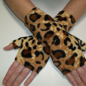 May include: A pair of fingerless gloves with a leopard print pattern. The gloves are made of a soft, tan fabric with brown and black spots. The gloves cover the hand up to the knuckles, leaving the fingers exposed.