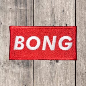 May include: A rectangular red patch with the word "BONG" in bold white letters. The patch has a red border and is set against a weathered wood background. The text is centered on the patch.