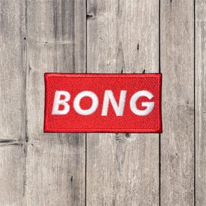 May include: A rectangular red patch with the word "BONG" in bold white letters. The patch has a red border and is set against a weathered wood background.