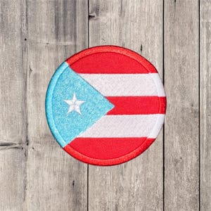 Peut inclure: Un écusson rond brodé représentant le drapeau de Porto Rico. Le motif comprend un triangle bleu clair avec une étoile blanche et des rayures rouges et blanches. L'écusson a une bordure rouge.