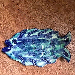May include: A blue and green ceramic fish shaped serving dish. The fish has a raised, textured surface and a slightly open mouth.