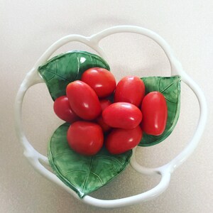 May include: A white ceramic bowl shaped like a flower with green leaves, holding a cluster of red tomatoes.