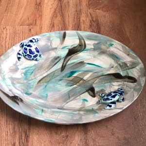 May include: An oval ceramic serving platter with a blue and white abstract design. Two small ceramic sea turtles are attached to the platter.
