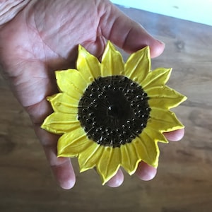 May include: A yellow ceramic sunflower dish with a brown center. The dish is hand-painted and has a rustic, handmade look.