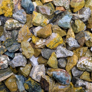 以下が含まれることがあります： 黄色、緑、グレー、茶色の様々なサイズの粗くカットされた岩のコレクション。一部の岩には、目に見える結晶構造と多様なテクスチャがあります。この品揃えは、造園や装飾目的の天然石のようです。