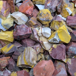 May include: A collection of raw, uncut rocks in various colors, including yellow, red, and white. The stones have a rough texture and irregular shapes, suggesting they are natural specimens. The image is a close-up, showcasing the variety of colors and patterns.