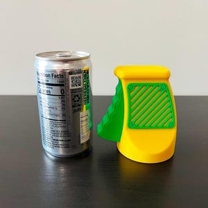 May include: A silver soda can next to a yellow and green can opener. The can opener has a yellow body with green accents and a green handle. The can has a nutrition facts label.
