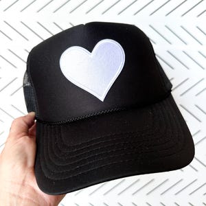 May include: A black trucker hat with a white heart patch on the front.