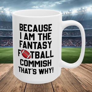 May include: White ceramic mug with the text "BECAUSE I AM THE FANTASY FOOTBALL COMMISH THAT'S WHY!" in black, with a red and white football graphic. The mug is on a wooden surface with a stadium background.