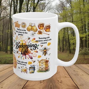 May include: White ceramic mug with a wraparound design featuring the words "Beekeeping Life" and illustrations of bees, honey pots, and a beehive. The mug has a large handle and is set against a blurred background.