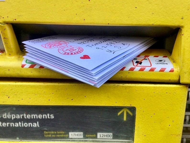 May include: A yellow metal mailbox with a red and white striped border. The mailbox has a slot for mail and a sign that says "d&eacute;partements international". The mailbox is labeled "La Poste" and has a sign that says "Derni&egrave;re lev&eacute;e lundi au vendredi 17H00 samedi 12H00".