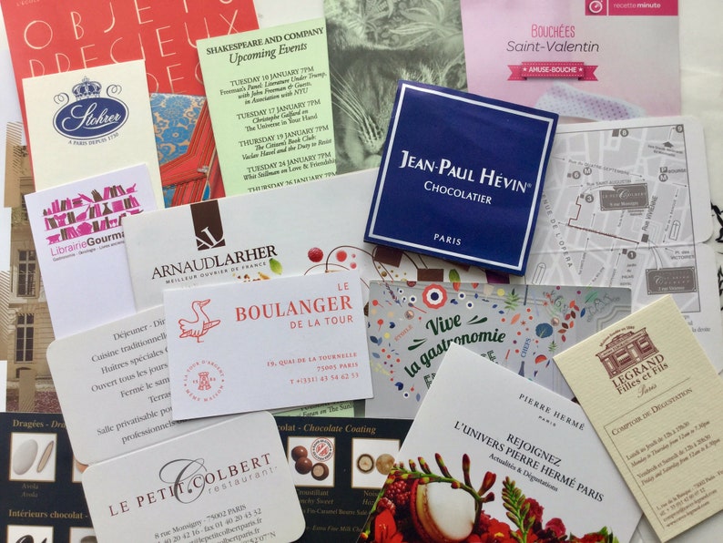 May include: A collection of various rectangular business cards and promotional flyers from Parisian establishments, including Jean-Paul H&eacute;vin, Le Boulanger de la Tour, and Pierre Herm&eacute;, featuring diverse typography, logos, and graphic illustrations.