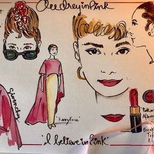 May include: A watercolor illustration of Audrey Hepburn in various poses, including a close-up of her face with red lipstick. The text "Audrey in Pink" and "I believe in pink" are written on the page. The illustration is a whimsical and colorful depiction of the iconic actress.
