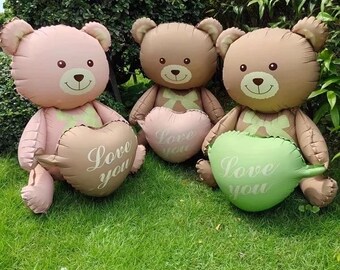 Può includere: Tre palloncini a forma di orsetto gonfiabili rosa, marroni e verdi, ciascuno con un palloncino a forma di cuore. Sui palloncini a forma di cuore c'è la scritta "Love you". Gli orsi sono seduti sull'erba verde.
