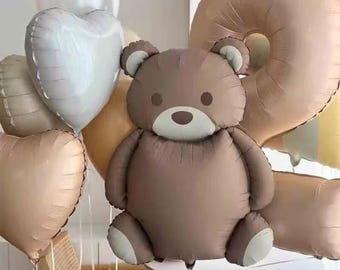 Può includere: Un palloncino a forma di orsetto marrone con dettagli bianchi, circondato da palloncini a forma di cuore e numero nei toni del bianco, beige e oro. I palloncini sono legati con un filo bianco, creando un'esposizione festosa.