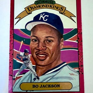 May include: A baseball card featuring Bo Jackson, a former professional baseball player. The card is red with a white border and features a colorful background with a baseball theme. The card is from the Donruss Diamond Kings series and features the Kansas City Royals logo.