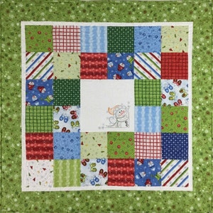 May include: A patchwork quilt with a green border and a white center featuring a snowman design. The quilt is made up of squares in various colors, including red, green, blue, and white.