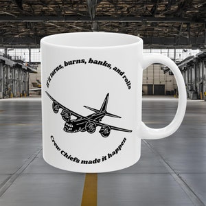 May include: White ceramic mug featuring a black illustration of a vintage airplane. The mug has the text "If it turns, burns, banks, and rolls" and "Crew Chiefs made it happen" in a circular design around the plane.