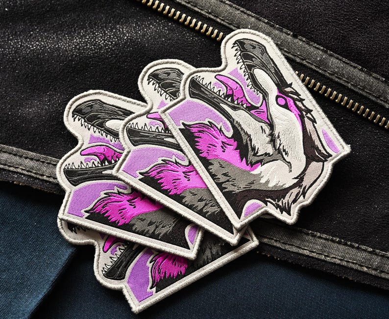 May include: Set of four embroidered patches featuring a pink and gray wolf with a purple background. The wolf's mouth is open and its teeth are visible. The patches are sewn onto a black leather jacket.