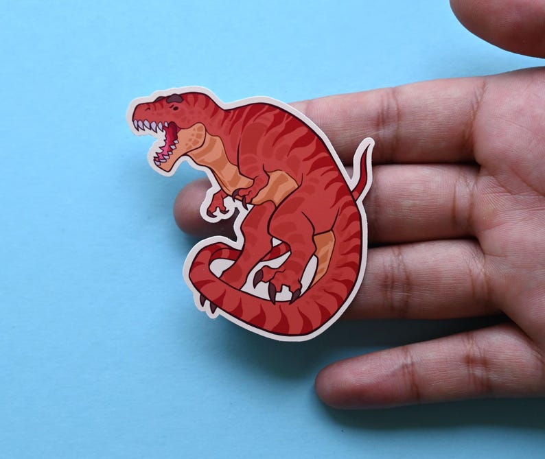 May include: Red dinosaur sticker with a curled tail and open mouth. The dinosaur is facing left and has a white outline.