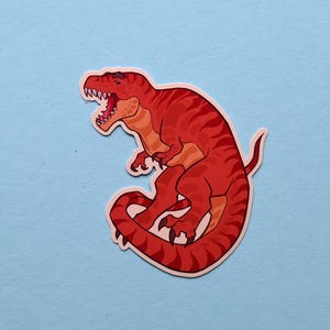 May include: Red dinosaur sticker with a curled tail and an open mouth. The dinosaur is outlined in black and has a white background.