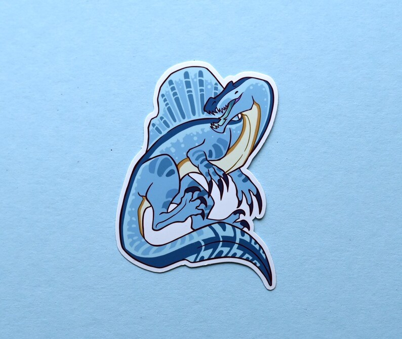 May include: A blue and white cartoon illustration of a Spinosaurus dinosaur with a large sail on its back. The dinosaur is depicted in a playful pose with its mouth open and its claws extended.