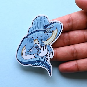 May include: A blue and white cartoon illustration of a Spinosaurus dinosaur with a large sail on its back. The dinosaur is depicted in a playful pose, with its mouth open and its tongue sticking out.