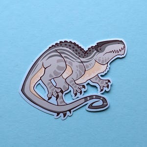May include: A gray and white dinosaur sticker with a striped pattern. The dinosaur has a long tail and a large head with sharp teeth.