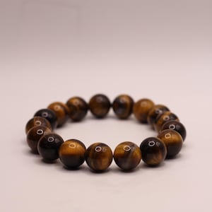 May include: A brown and gold tiger's eye beaded bracelet. The bracelet is made of round beads and is strung on a clear elastic cord.