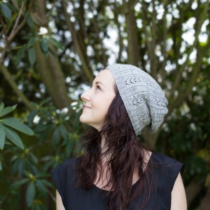 Könnte beinhalten: Eine Frau trägt eine graue Strickmütze mit einem Spitzenmuster und blickt zum Himmel. Sie trägt ein schwarzes ärmelloses Oberteil und hat lange braune Haare.