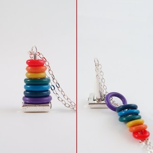 May include: A silver chain necklace featuring a pendant shaped like a colorful stack of rings. The rings are in rainbow colors: red, orange, yellow, green, blue, and purple. The pendant is attached to a delicate silver chain.