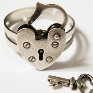 May include: A silver ring featuring a heart-shaped padlock design. The padlock has a keyhole and is connected to a double-banded ring. A small key is placed nearby. This ring is a unique piece of jewellery.