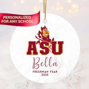 May include: A round, white ceramic ornament with a gold string for hanging. The ornament features the letters "ASU" in maroon and gold, a devil mascot, and the name "Bella" with "Freshman Year 2025" below. A red banner reads "PERSONALIZED FOR ANY SCHOOL."