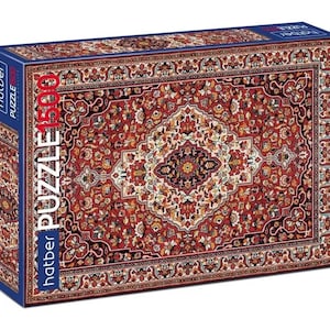 May include: A puzzle box displaying a detailed Persian rug design. The rug is mainly red, with cream, gold, and black floral patterns. The box has the text "hatber PUZZLE 1500". The box is rectangular.
