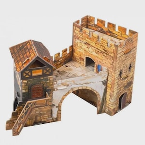 May include: A miniature medieval castle model with a stone facade, featuring a tower, arched gateway, and a small building with a wooden staircase. The model has a detailed design with a brown roof and a weathered appearance.