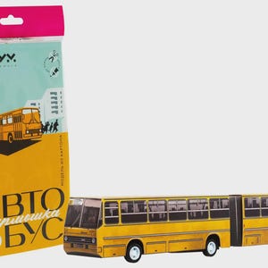 Peut inclure: Un modèle de bus articulé jaune, avec un design détaillé, est présenté à côté de son emballage. L'emballage présente une illustration de bus et du texte en langue étrangère. Le modèle est à l'échelle 1:87.