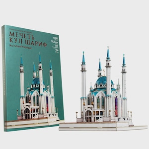 May include: A model of the Kul Sharif Mosque, featuring white walls, blue domes, and tall minarets. The model is accompanied by a box with the mosque's name in Russian and English, along with scale and size details. The model is approximately 7.7 inches in length.