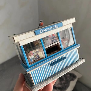 Puede incluir: Un modelo en miniatura de un quiosco azul y blanco a rayas con un letrero que dice "Союзпечати" y un peque&ntilde;o p&aacute;jaro posado en la parte superior.
