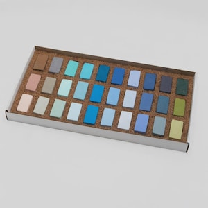 Puede incluir: Una caja rectangular de cartón blanco que contiene treinta y dos barras de pastel rectangulares dispuestas en cuatro filas. Las barras presentan una variedad de colores que incluyen tonos de azul, verde, marrón, gris y beige, sobre paja marrón.