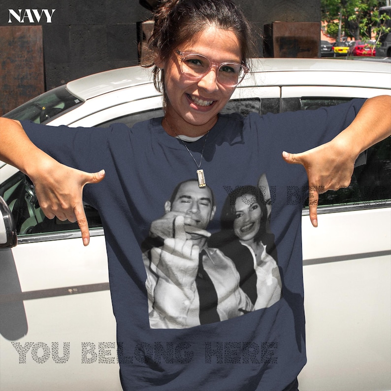 May include: A navy blue t-shirt with a photo of Barack Obama and Michelle Obama. The text "You Belong Here" is printed on the shirt.