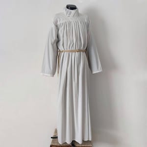 May include: A light gray, long-sleeved robe with a high collar and a rope belt. The robe has a flowing design and is displayed on a mannequin. The sleeves are long and the hem reaches the floor. The robe is made of a soft fabric.