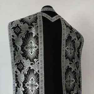May include: Black liturgical vestment with silver floral and geometric patterns on the edges.