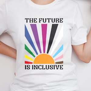 Könnte beinhalten: Weißes T-Shirt mit dem schwarzen Text "THE FUTURE IS INCLUSIVE". Das Design zeigt einen farbenfrohen Sonnenaufgang mit Regenbogenstrahlen und einer orangefarbenen Sonne. Das Shirt ist aus weichem Material.