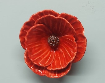 May include: A ceramic poppy flower with a red glaze. The flower has multiple layers of petals and a brown center.